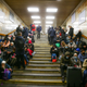 Many people sit on either side of a stairwell in a fluorescent-lit subway station in Ukraine.